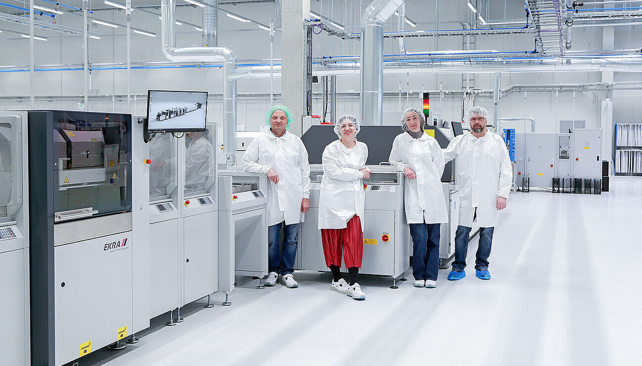 Vier Personen mit weißen Kittel vor und neben Maschinen in einer Produktionshalle.