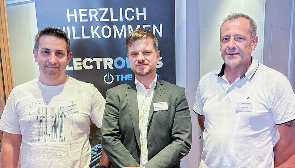 Drei Männer stehen lächelnd nebeneinander.